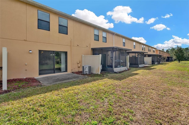 rear view of house with central AC unit, a yard, a sunroom, and a patio