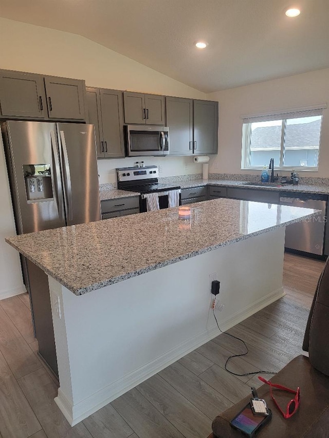 kitchen with lofted ceiling, sink, appliances with stainless steel finishes, a center island, and light stone countertops