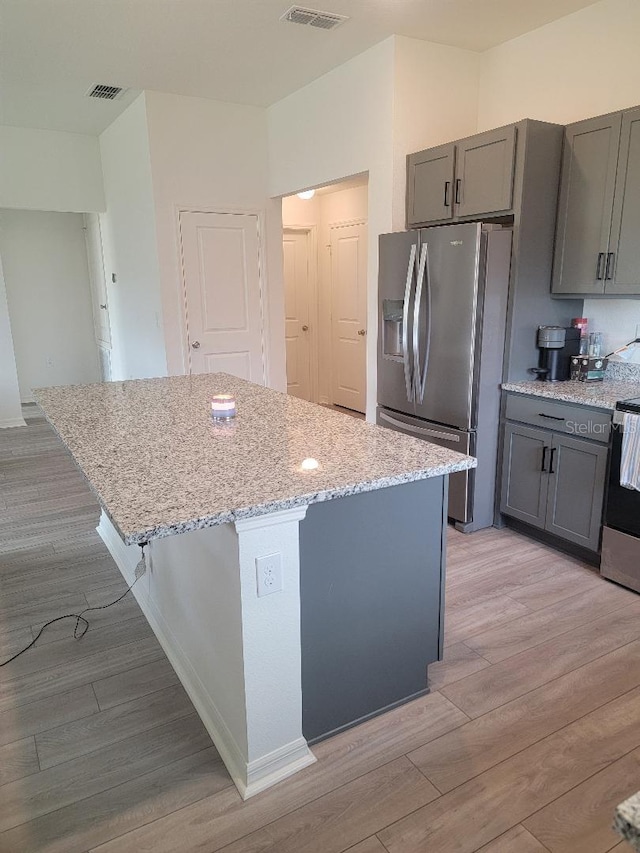 kitchen with gray cabinets, a kitchen island, appliances with stainless steel finishes, light stone counters, and light hardwood / wood-style floors