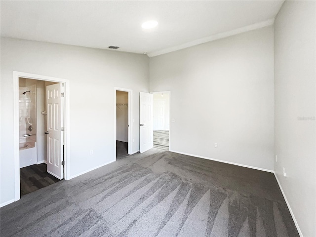 unfurnished bedroom featuring connected bathroom, dark carpet, a walk in closet, and a closet