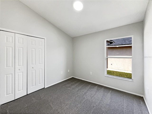 unfurnished bedroom with dark carpet, vaulted ceiling, and a closet