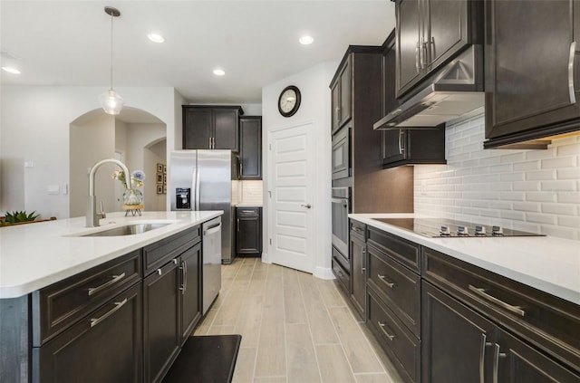 kitchen featuring sink, hanging light fixtures, light wood-type flooring, appliances with stainless steel finishes, and backsplash