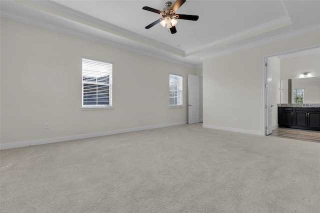 unfurnished living room featuring a raised ceiling, ornamental molding, light carpet, and ceiling fan