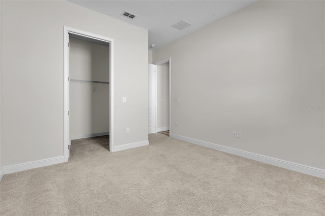 unfurnished bedroom with a walk in closet, a closet, and light carpet