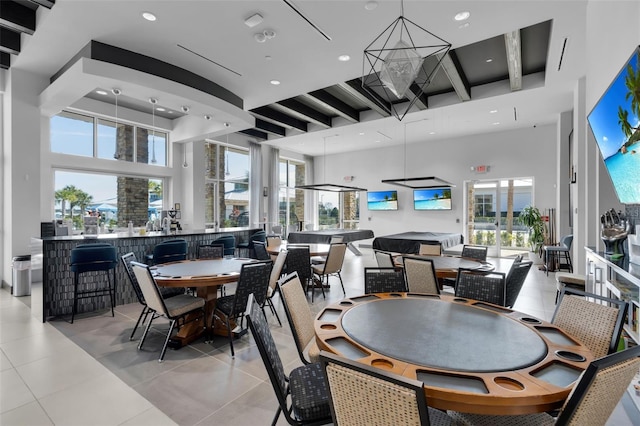 dining area with a healthy amount of sunlight, beam ceiling, light tile patterned floors, and a high ceiling