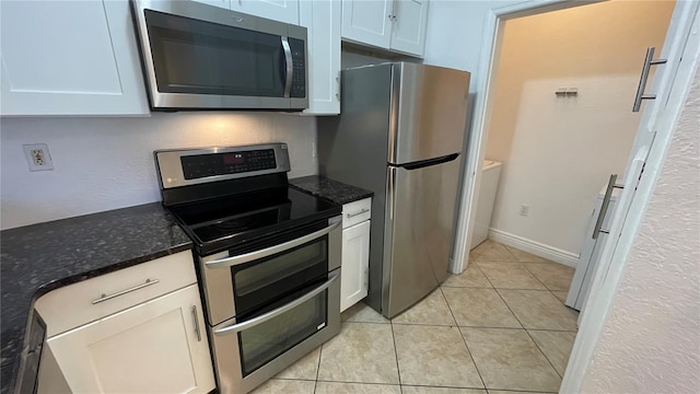 kitchen with white cabinetry, light tile patterned floors, stainless steel appliances, and dark stone counters