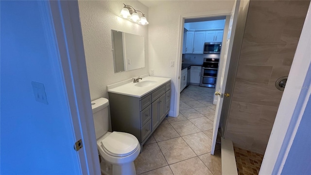 bathroom with tiled shower, vanity, toilet, and tile patterned flooring