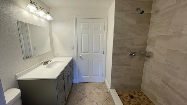 bathroom with tile patterned flooring, vanity, tiled shower, and toilet