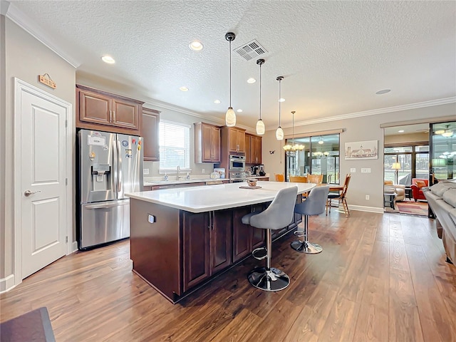 kitchen with pendant lighting, dark wood-type flooring, appliances with stainless steel finishes, a kitchen breakfast bar, and a kitchen island