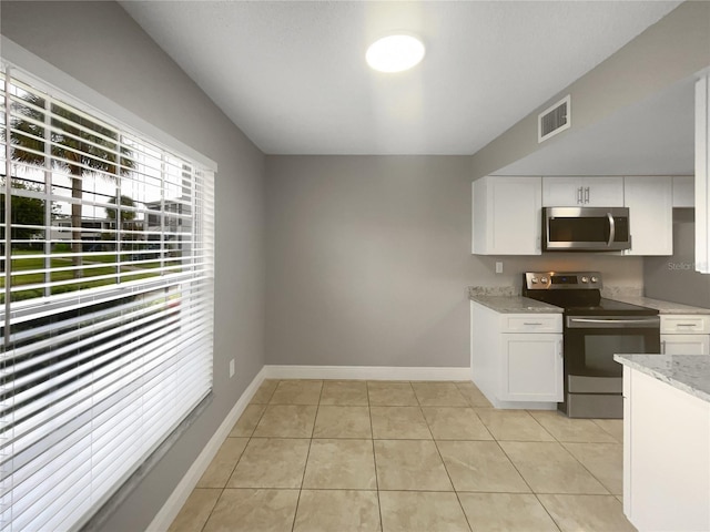 kitchen with white cabinetry, stainless steel appliances, light stone countertops, and light tile patterned floors