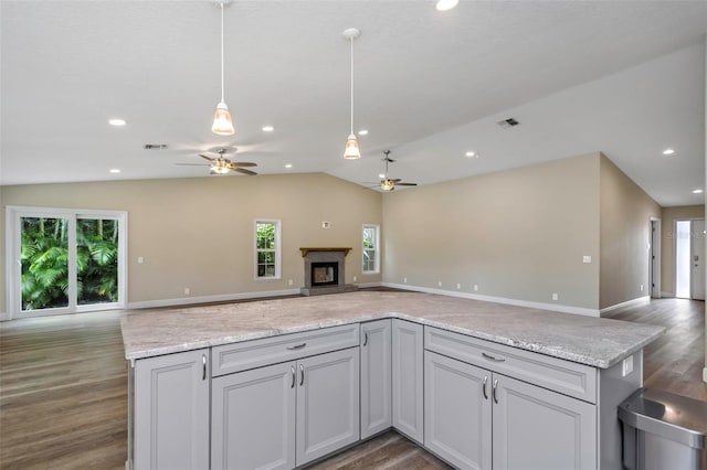 kitchen with decorative light fixtures, lofted ceiling, light stone counters, a premium fireplace, and dark wood-type flooring