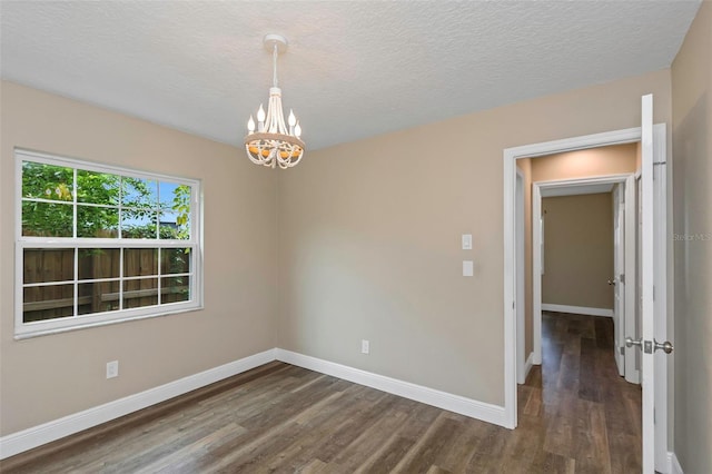 empty room with dark wood-type flooring, a chandelier, and a textured ceiling