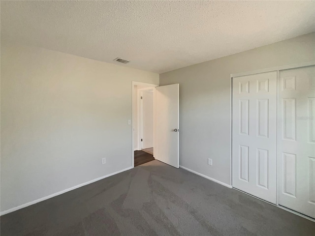 unfurnished bedroom featuring dark colored carpet, a closet, and a textured ceiling