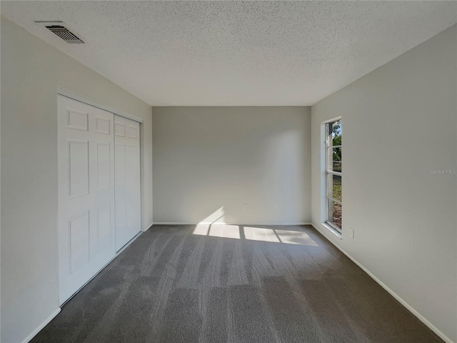 unfurnished bedroom with a closet, dark carpet, and a textured ceiling