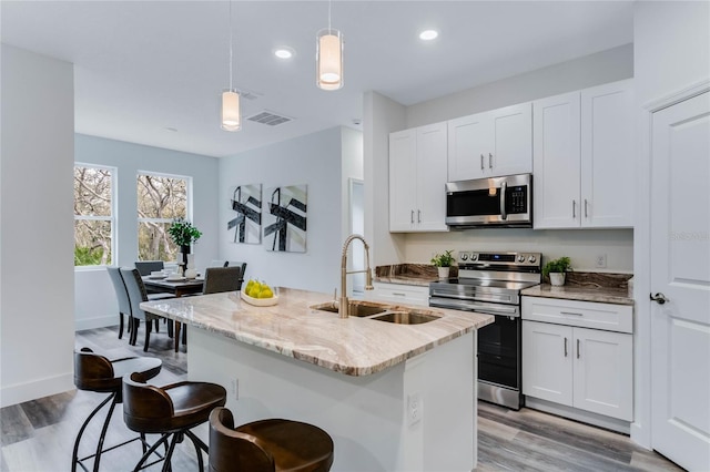 kitchen with appliances with stainless steel finishes, decorative light fixtures, sink, white cabinets, and a kitchen island with sink