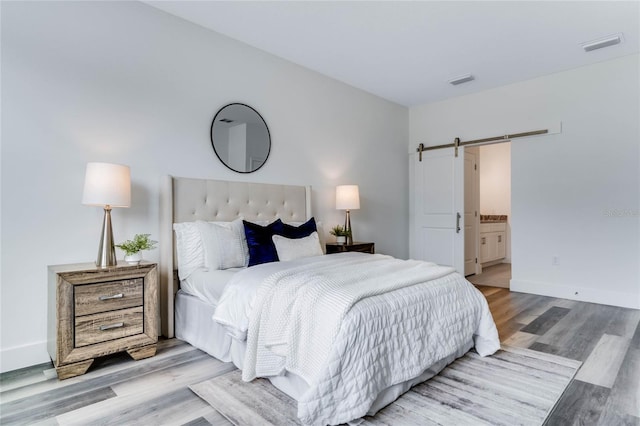 bedroom with a barn door, connected bathroom, and light hardwood / wood-style flooring