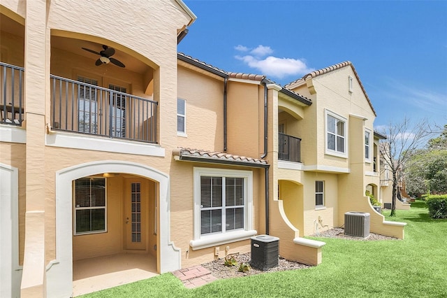 back of property featuring ceiling fan, a balcony, a yard, and central air condition unit