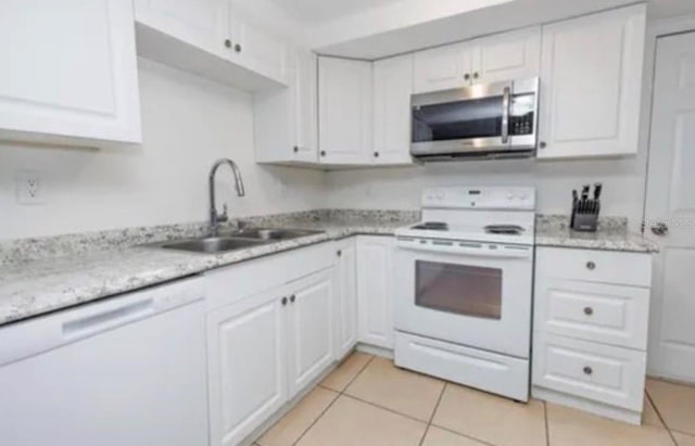 kitchen with light stone counters, white cabinetry, a sink, light tile patterned flooring, and white appliances