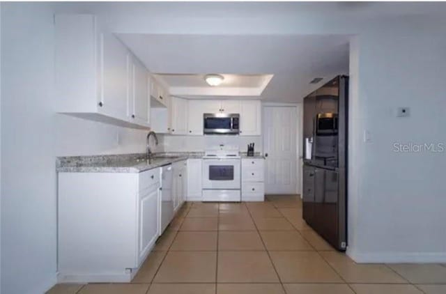 kitchen with white appliances, a sink, white cabinetry, light countertops, and a raised ceiling