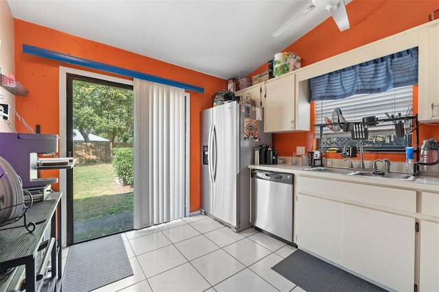 kitchen with lofted ceiling, sink, light tile patterned floors, white cabinetry, and stainless steel appliances