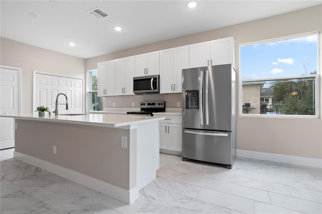 kitchen with a wealth of natural light, stainless steel appliances, white cabinets, and a center island with sink