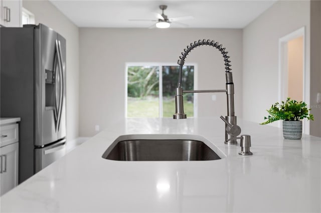 kitchen featuring white cabinetry, sink, ceiling fan, stainless steel refrigerator with ice dispenser, and light stone countertops