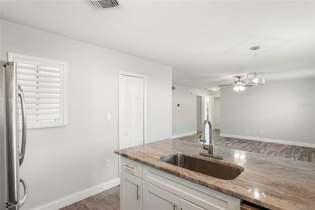 kitchen featuring sink, white cabinets, stainless steel fridge, hanging light fixtures, and light stone countertops