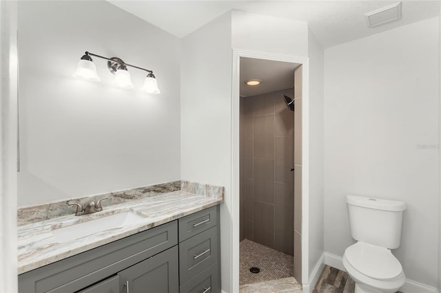 bathroom with tiled shower, vanity, and toilet