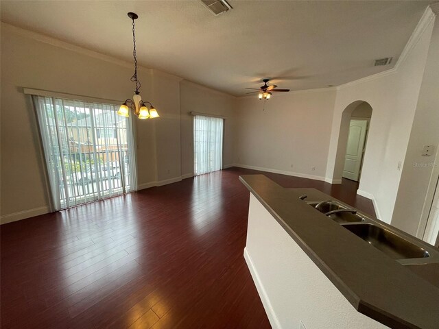 spare room featuring dark wood-type flooring, crown molding, ceiling fan with notable chandelier, and sink