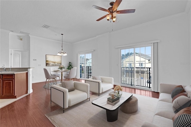 living area with ornamental molding, a textured ceiling, wood finished floors, baseboards, and ceiling fan with notable chandelier