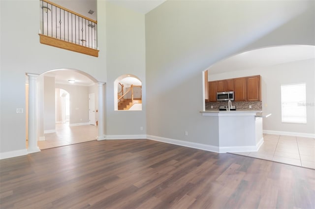 unfurnished living room featuring light hardwood / wood-style flooring, decorative columns, and a high ceiling