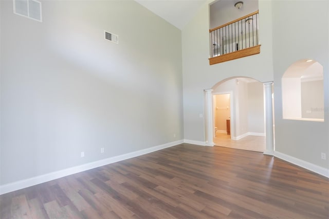 empty room featuring dark hardwood / wood-style flooring, a towering ceiling, and ornate columns