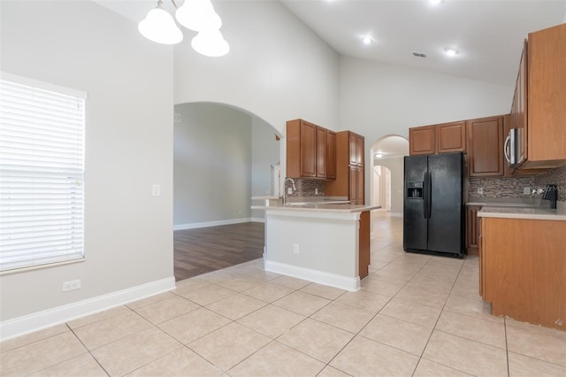 kitchen with light tile patterned floors, an inviting chandelier, backsplash, black fridge, and decorative light fixtures