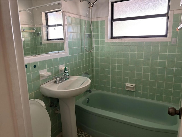 full bathroom featuring tiled shower / bath, plenty of natural light, toilet, and tile walls