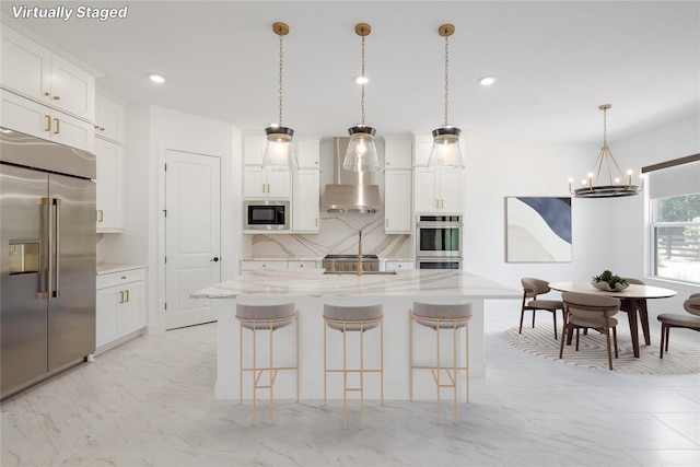 kitchen featuring built in appliances, light stone countertops, white cabinets, a center island with sink, and decorative light fixtures