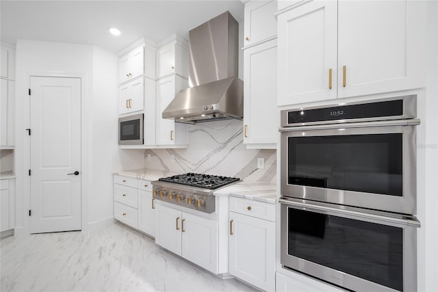 kitchen with stainless steel appliances, wall chimney range hood, white cabinets, and light stone counters