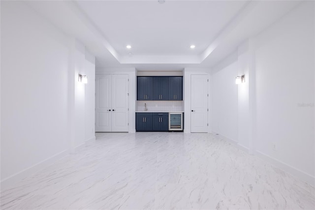 unfurnished living room featuring wine cooler, wet bar, and a raised ceiling