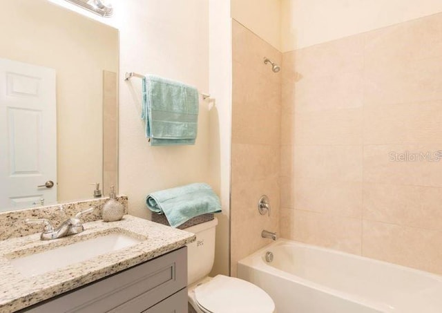 full bathroom with tiled shower / bath, vanity, and toilet