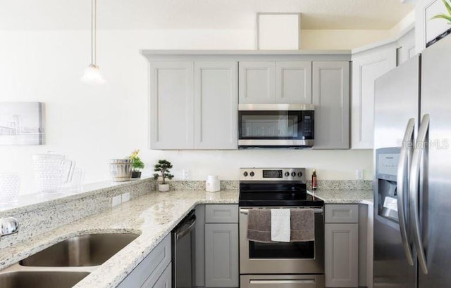 kitchen with gray cabinetry, pendant lighting, light stone countertops, and appliances with stainless steel finishes