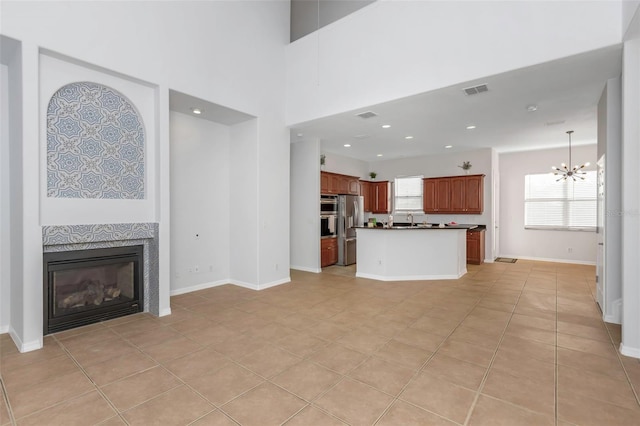 unfurnished living room featuring light tile patterned floors, sink, a high ceiling, a fireplace, and a chandelier