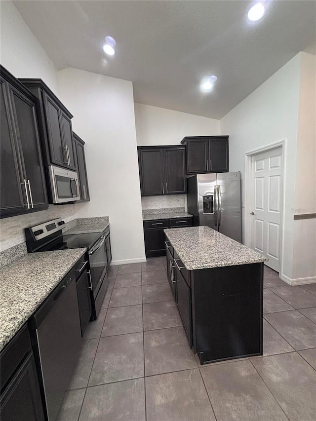 kitchen featuring appliances with stainless steel finishes, tile patterned flooring, light stone countertops, a kitchen island, and vaulted ceiling