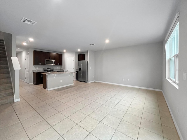 kitchen with a kitchen bar, dark brown cabinets, light tile patterned floors, an island with sink, and stainless steel appliances