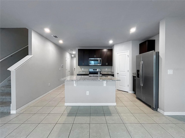 kitchen featuring sink, appliances with stainless steel finishes, a center island with sink, light stone countertops, and light tile patterned flooring