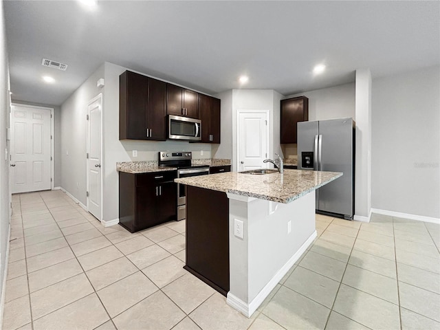 kitchen featuring sink, light tile patterned floors, stainless steel appliances, dark brown cabinets, and a center island with sink