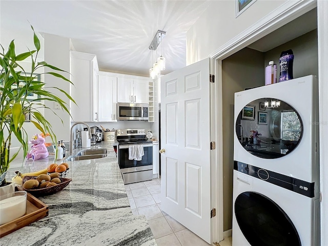 kitchen featuring white cabinetry, light stone counters, stacked washer and clothes dryer, and appliances with stainless steel finishes