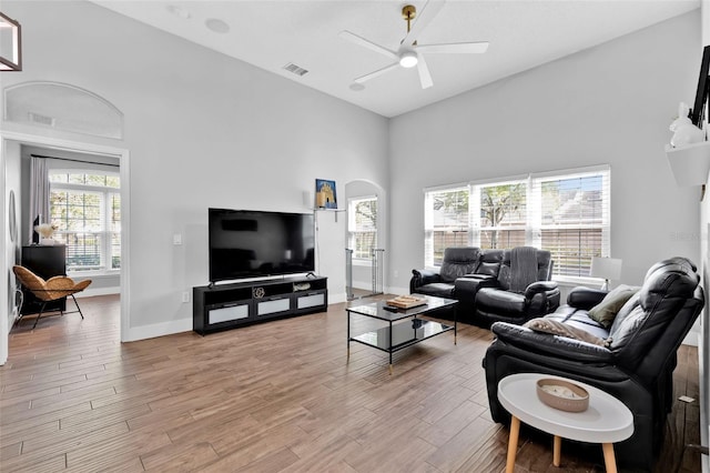 living room featuring a towering ceiling, ceiling fan, and light hardwood / wood-style flooring