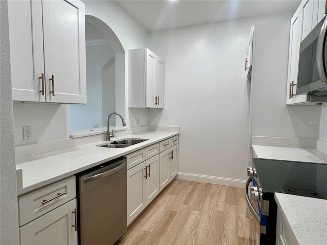 kitchen with stainless steel appliances, white cabinetry, sink, and light stone counters