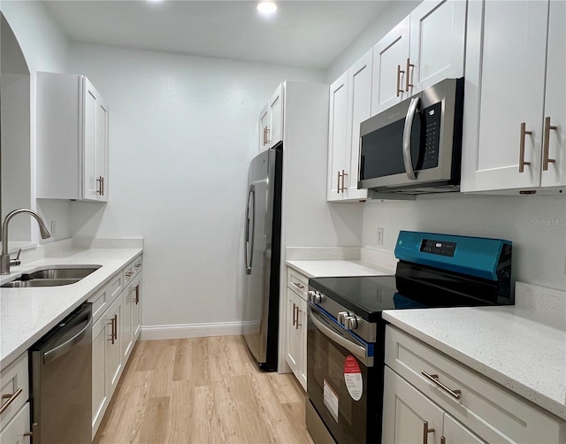 kitchen featuring light stone counters, a sink, white cabinetry, appliances with stainless steel finishes, and light wood-type flooring