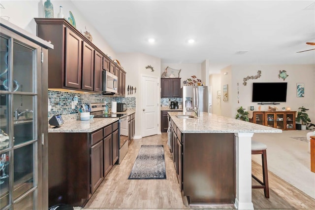 kitchen with appliances with stainless steel finishes, a breakfast bar, dark brown cabinets, and backsplash