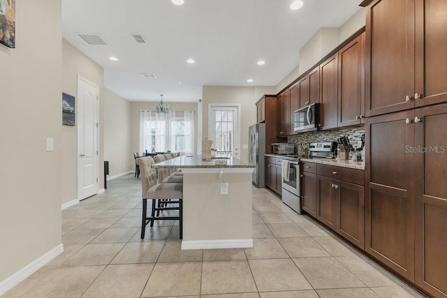 kitchen with a breakfast bar area, light stone counters, stainless steel appliances, a kitchen island with sink, and backsplash